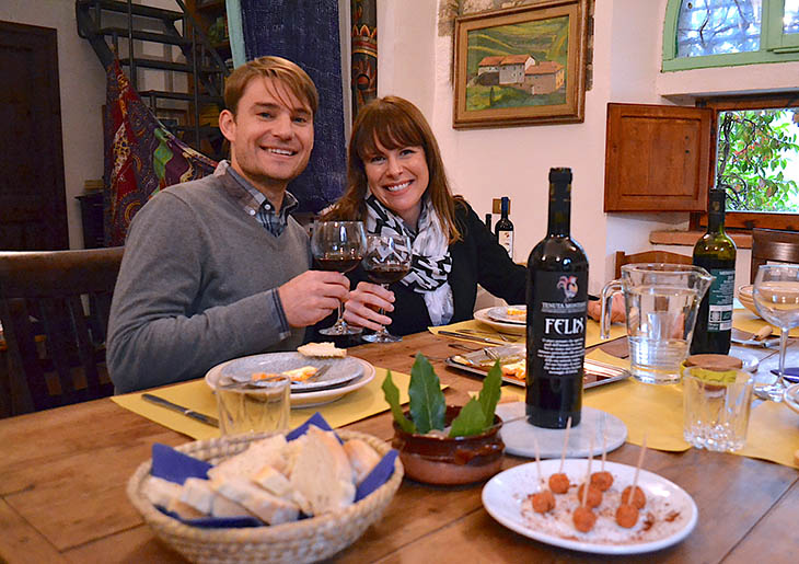 Couple of young people toasting with chianti in front of a table set for a typical Tuscan lunch
